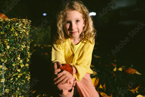 Quadro su tela Smiling little girl holding autumn leaf at night in dramatic light outdoors
