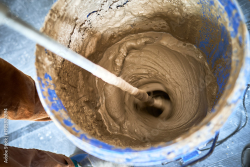 Close up of electric paddle mixer blending plaster or cement texture mix in a blue bucket for construction and renovation work. Diy and home improvements. Thick cement paste.