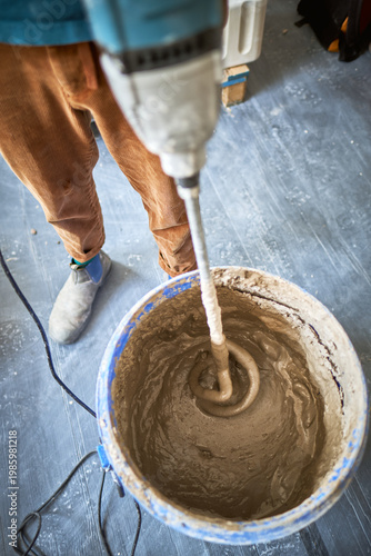 Close up of electric paddle mixer blending plaster or cement texture mix in a blue bucket for construction and renovation work. Diy and home improvements. Thick cement paste.