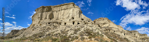 exterior of old troglodyte dwellings bordered by a road in the Bardenas desert in Spain  under blue sky