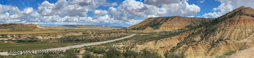 panoramic view of the Bardenas desert crossed by a road with its sandstone hills under a blue sky and white clouds
