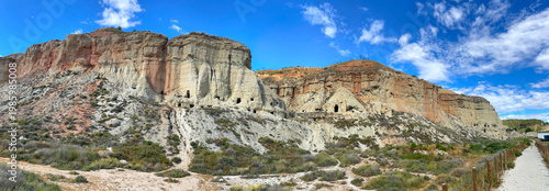 exterior of old troglodyte dwellings bordered by a road in the Bardenas desert in Spain  under blue sky