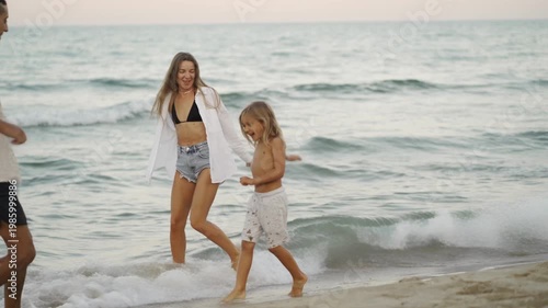A smiling woman in casual summer attire splashes water at a child on a sandy beach, both enjoying the refreshing sea. The playful scene captures the essence of a happy summer vacation