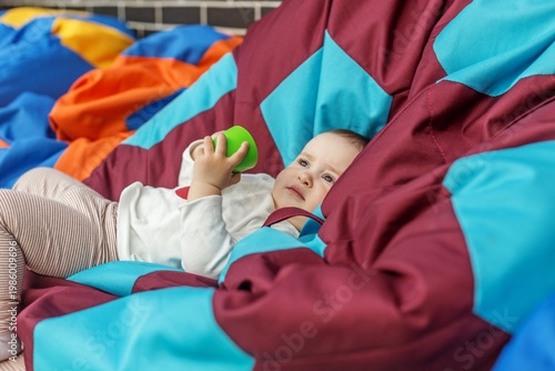 Toddler relaxing on bean bag and playing with toy cup. Early years.