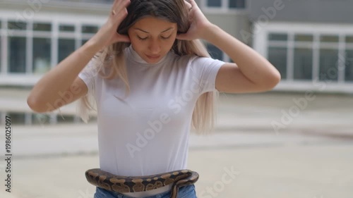 Young woman holding python snake around her waist in abandoned urban environment, wild animal concept