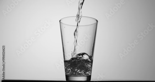 Slow-motion stream of water pouring into a transparent glass, forming bubbles and rising turbulence against a clean minimal background with copy space