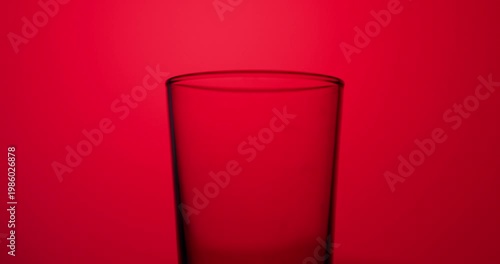 Slow-motion water stream pouring into a clear glass, creating bubbles and turbulence against a bold red illuminated background with strong contrast and copy space