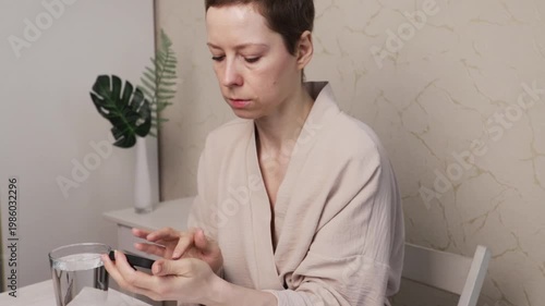 woman checks smartphone reminder with water glass, managing medication routine and follow-up plan