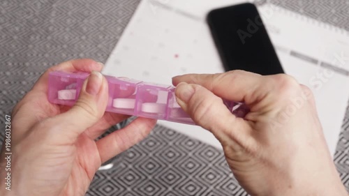 hands remove a pill from organizer with smartphone and calendar background, adherence routine
