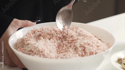 a spoon lifting long grain basmati rice lightly tinted with red seasoning, highlighting texture and spice distribution during preparation of a savory rice dish