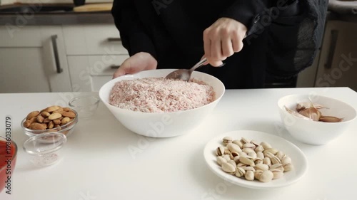 hands mix white basmati rice with red seasoning in a large bowl while almonds pistachios and garlic sit nearby, capturing a colorful prep stage of a festive main dish