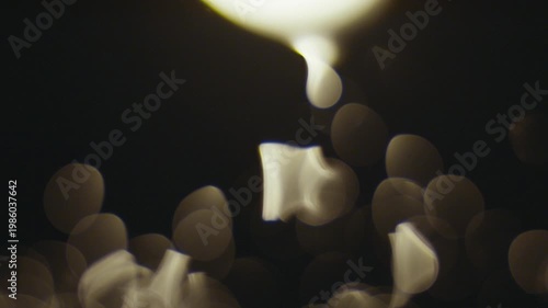 Blurry image of bokeh lights against dark background with white shapes floating