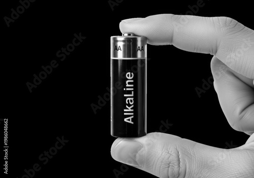 Closeup of a hand holding a single aa alkaline battery against a dark background, symbolizing power and energy storage