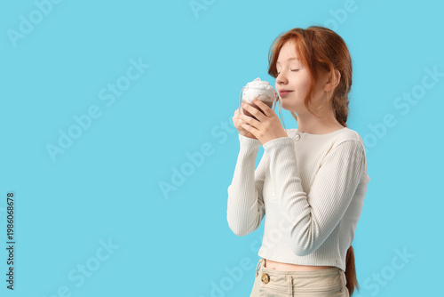 Teenage redhead girl drinking sweet cocoa on blue background