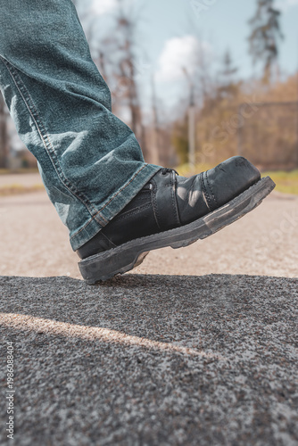 Brutal biker boot. Black thick leather. Blue jeans. Scratches and road dust on the shoe. Brutal style. Motorcycle theme. Spirit of freedom. Road adventures. Motorcycle trip. Garage poster. 