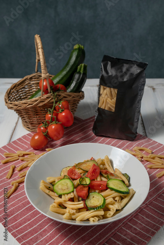 A plate of pasta, caserecce with tomato and courgettes, with a half-kilo pack and the ingredients used nearby