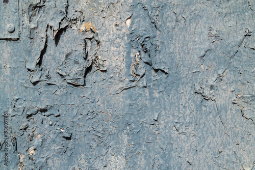 The blue paint on an old metal surface is heavily peeling and cracked, revealing a lighter color underneath.