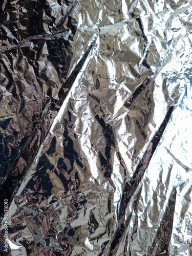 Abstract crumpled silver aluminum foil texture, shiny metallic background with deep wrinkles and light reflections, grey surface detail
