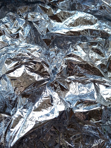 Abstract crumpled silver aluminum foil texture, shiny metallic background with wrinkles and light reflections, grey surface detail
