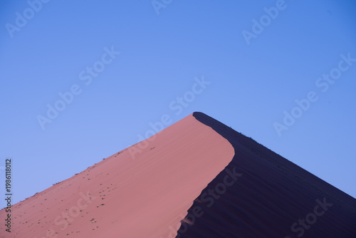 Golden dunes rise like waves frozen in time, stretching endlessly under a sky painted with soft pastels, where solitude and silence reveal the raw soul of Namibia’s desert.	
