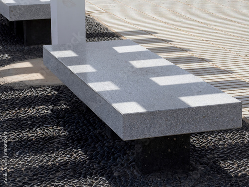 Modern concrete bench casting strong geometric shadows on tiled ground creating abstract light and shadow pattern outdoors