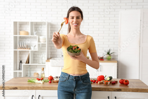 Slika na platnu Beautiful young woman with bowl of fresh vegetable salad in kitchen
