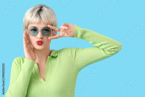 Portrait of beautiful young woman with sunglasses showing victory gesture on ...