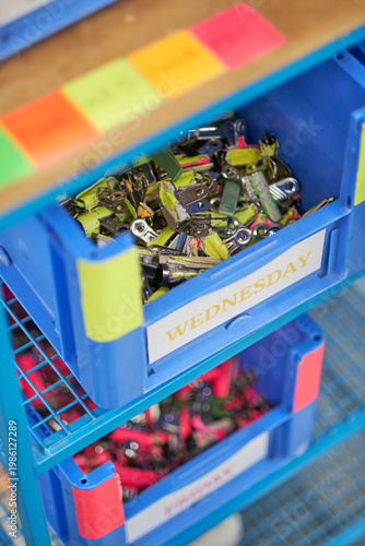 Plastic storage bin filled with colour coded metal binder clips in workshop organisation system close up. Organisation colour tagging.