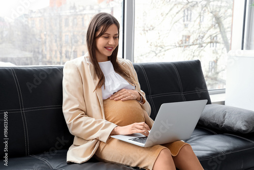 Beautiful pregnant businesswoman working with laptop on couch in office