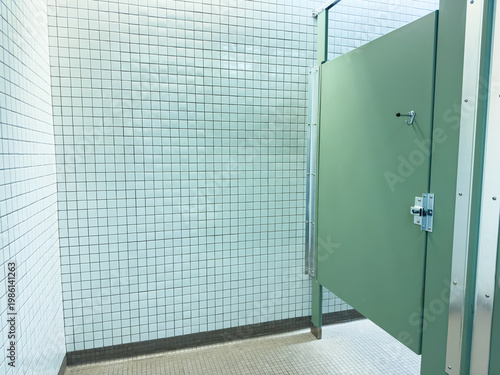 Fotografie Bathroom stall with green door and tiled walls in public restroom during daytime