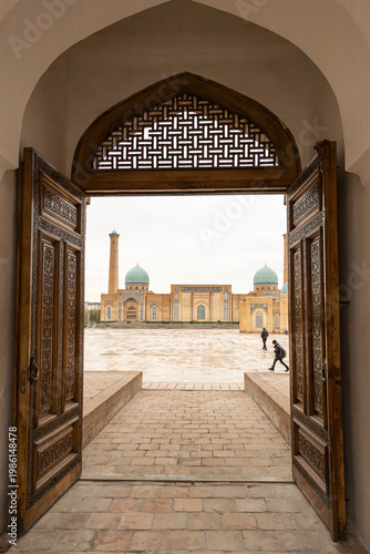Khast-Imam Mosque and Hazrati Imam square with strolling people framed by ornate wooden Doorway of Barak Khan Medrese. Hazrati Imam Complex in Tashkent, Uzbekistan.