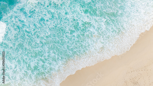 Aerial view of turquoise ocean water meets foamy waves at the sandy shoreline. La Digue, Seychelles.