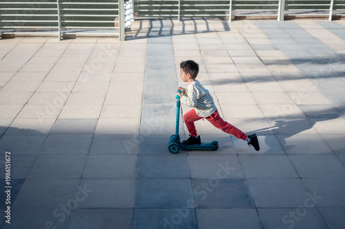 Young Boy Riding a Scooter on a Sunlit Pavement, Enjoying Outdoor Playtime