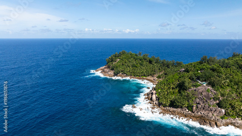 Turquoise waters meet a rocky shoreline, surrounded by dense green foliage and scenic views. Seychelles, Mahe.