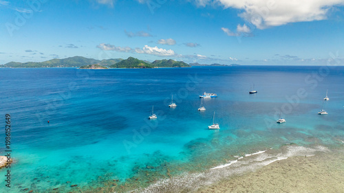 Anchored boats on turquoise waters with distant green islands and a clear blue sky. La Digue, Seychelles.