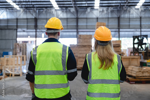 Foto Caucasian workers conduct warehouse inspection amidst stacked boxes and wooden pallets in busy industrial setting with high-visibility vests