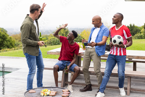 Photos Four male friends gathering on wooden deck by pool, using barbecue grill and hol