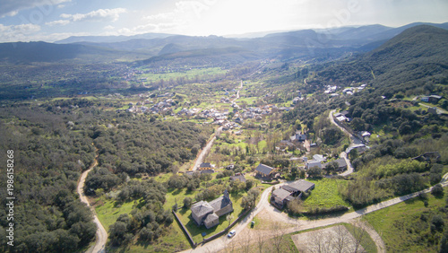 Aerial view from the Hermitage of the Virgin of the Star crowning the town of San Juan de Paluezas amidst forests and vegetation, framing a typical Bierzo landscape of villages nestled among mountains