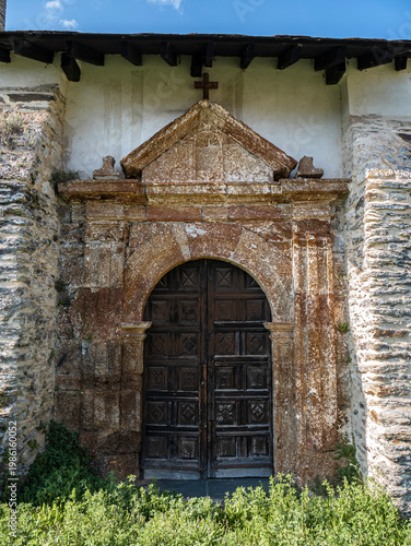 Old wooden door in a cross arch surrounded by carved stone and a cross at the top belonging to the parish church of San Juan de Paluezas - Our Lady of the Assumption