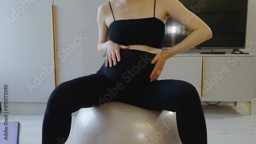 Maternal health care and sports gymnastics to relax birth canal. Mother-to-be takes care of her body and baby, doing morning exercises on a fitball at home. Pregnant woman sits on a ball. Close-up.