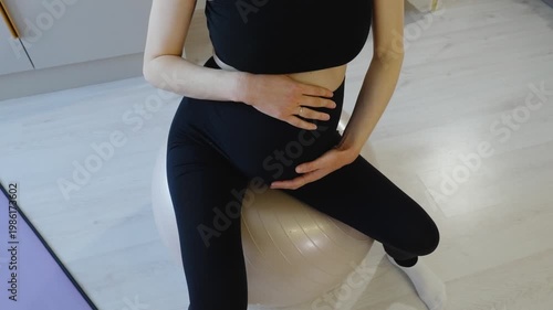 Fitness for pregnant women. Upper left view of pregnant woman's belly sitting on fitball. Close-up of pregnant woman's belly during exercises. Preparing for childbirth in seventh month of pregnancy.