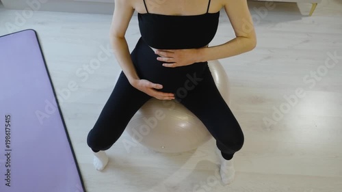 Maternal health care and sports gymnastics to relax birth canal. Mother-to-be takes care of her body and baby, doing morning exercises on a fitball at home. Pregnant woman sits on a ball. Top view.