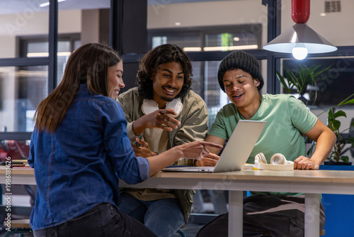 Diverse students leaning in, discussing group project at study lounge with laptop and headphones