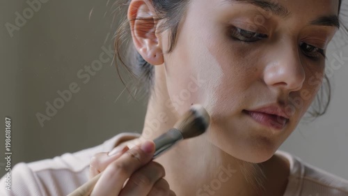 Woman applying makeup with a brush on her cheek face closeup