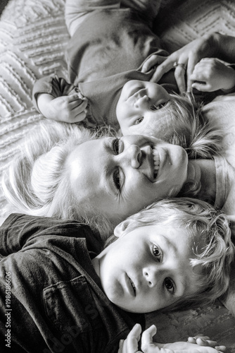 Smiling mother and two young children lying together on a bed, sharing a joyful family moment.