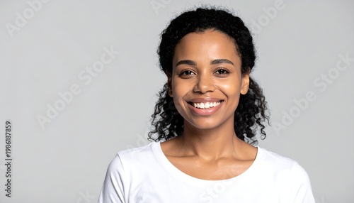 Smiling, dark-haired woman with flawless skin in a white tee against a solid light gray backdrop