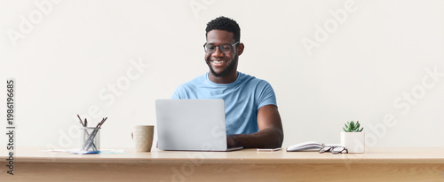 Photos A man sits at a wooden desk working on a laptop