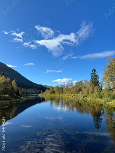 Serene river reflecting autumn trees and blue sky in the Scandinavian wilderness