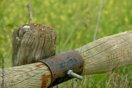 Poste de valla de madera con piezas metálicas en primer plano, con silueta que recuerda a un pájaro imaginario de alas abiertas.