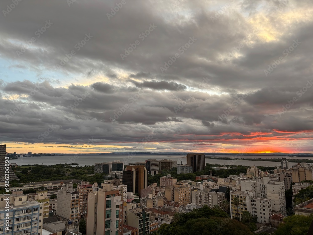 Fototapeta premium Wide panoramic view of Porto Alegre skyline with dramatic clouds and orange sunset horizon